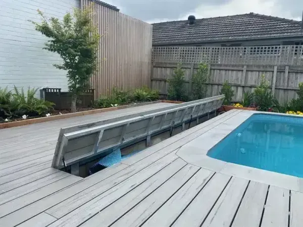 Pool area with open deck cover, wood deck, and surrounding landscaping.
