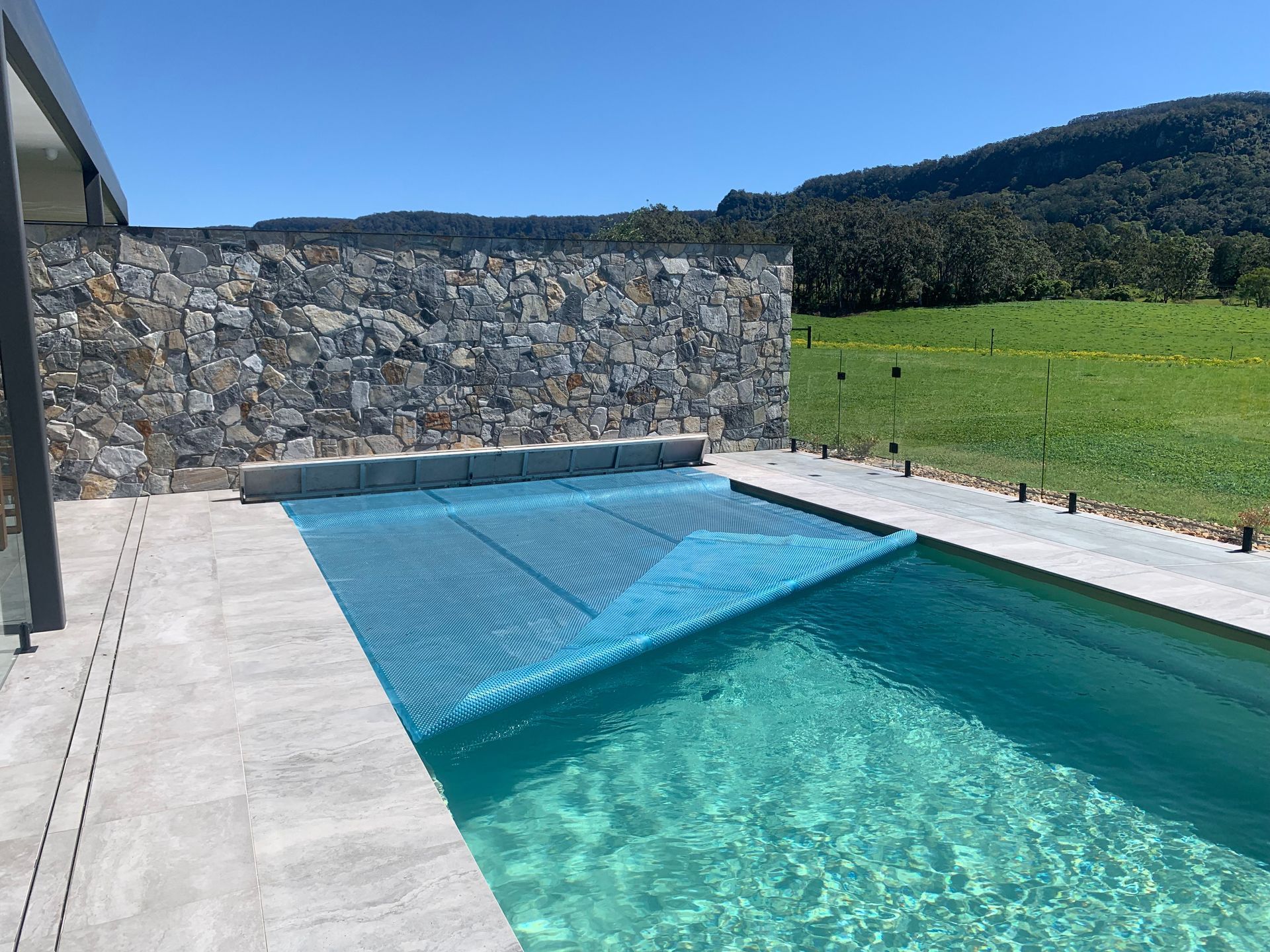 Pool with blue water and cover, glass fence, and ocean view.