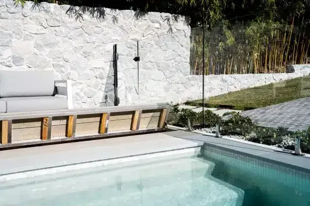 Poolside outdoor space with a white stone wall, pool, seating, and bamboo.