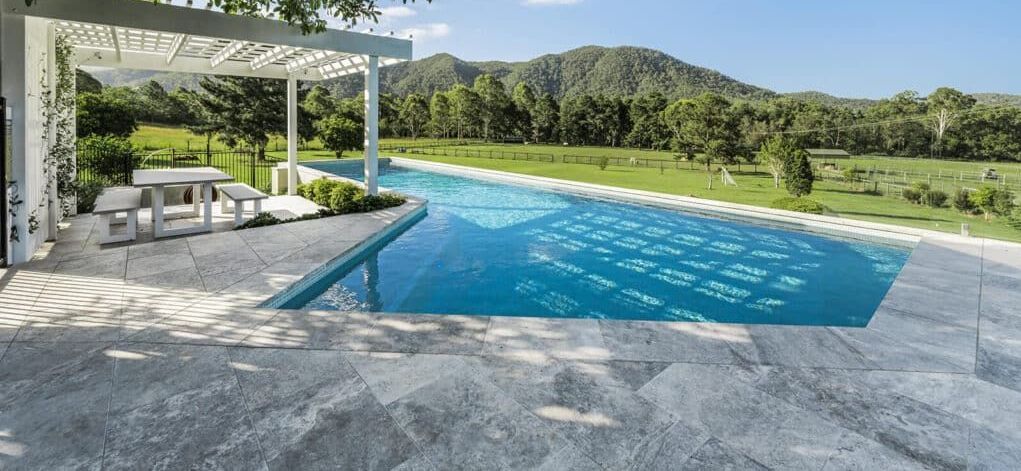An infinity pool with a view of a mountain and lush green field.