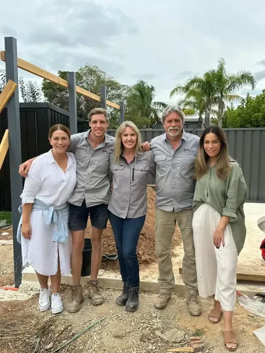 Five people stand outside a building site, smiling. Construction materials are visible.