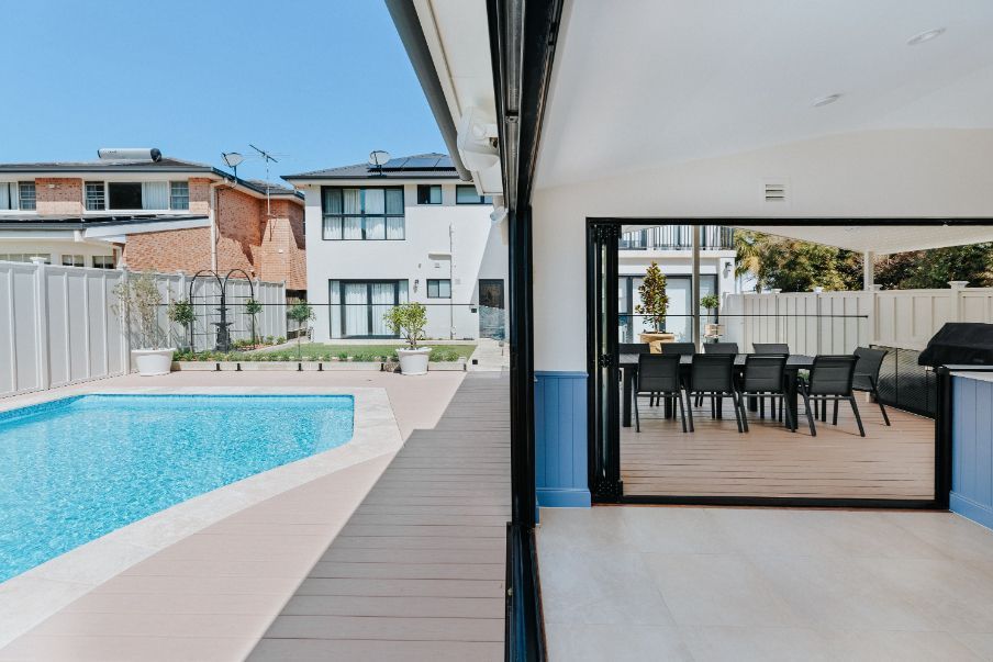 Pool, deck, and dining area open to backyard. Blue sky and sunny day.