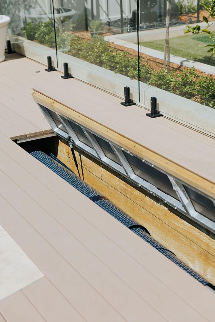 Deck with a section open, revealing a windowed structure below, next to a glass railing.