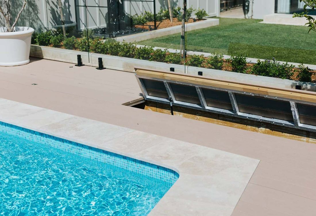 Pool with light-colored coping, blue water, and tan decking. A retractable cover is partially open near a green lawn.