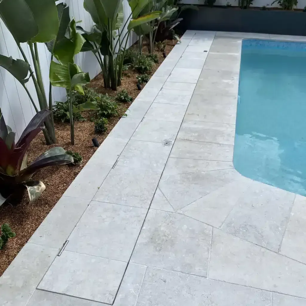 Poolside with stone coping, plants, and a water-filled pool.