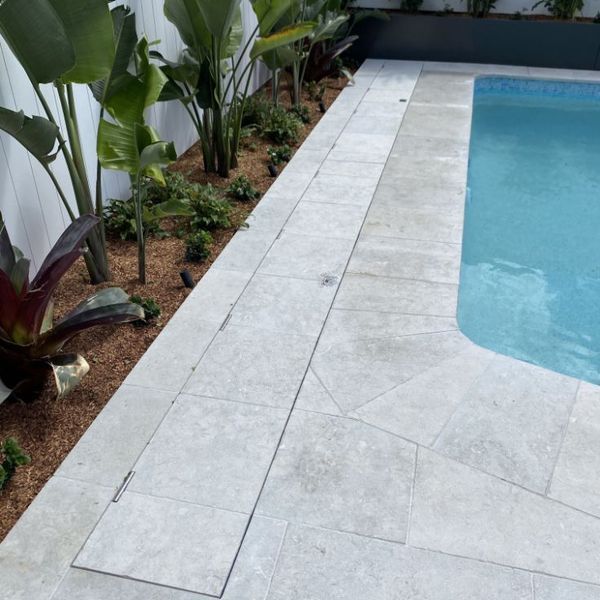 Poolside with light gray tiles, plants, and pool.