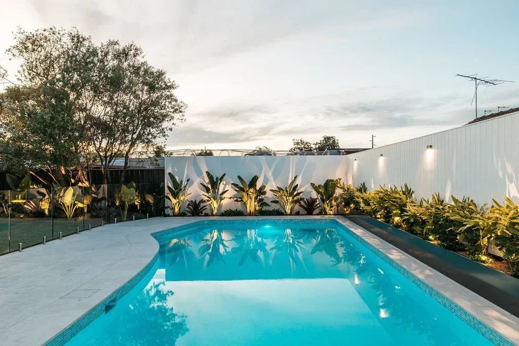 Swimming pool in backyard with white fence, plants, and cloudy sky.