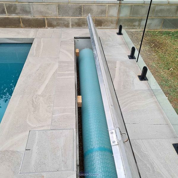 Pool cover rolled up inside a recessed compartment next to a pool.