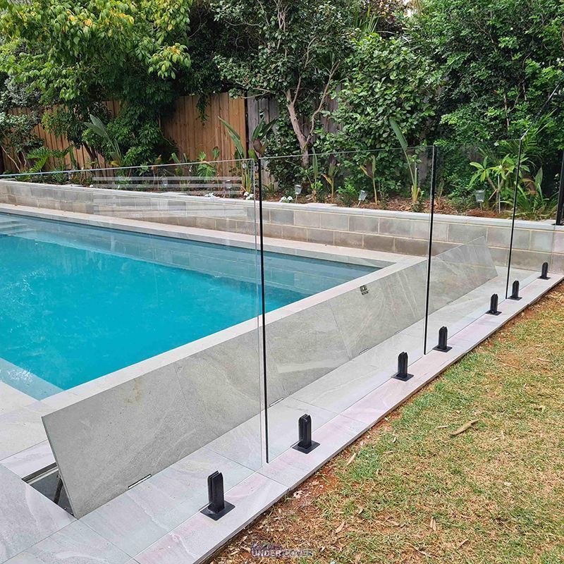 Pool area with glass fence, tiled surrounds, and greenery.
