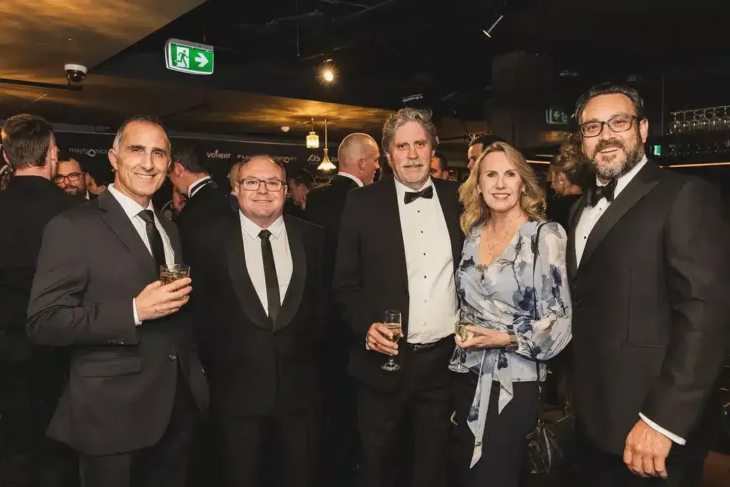 Group of five people in formal attire, inside a dimly lit venue, smiling and holding drinks.