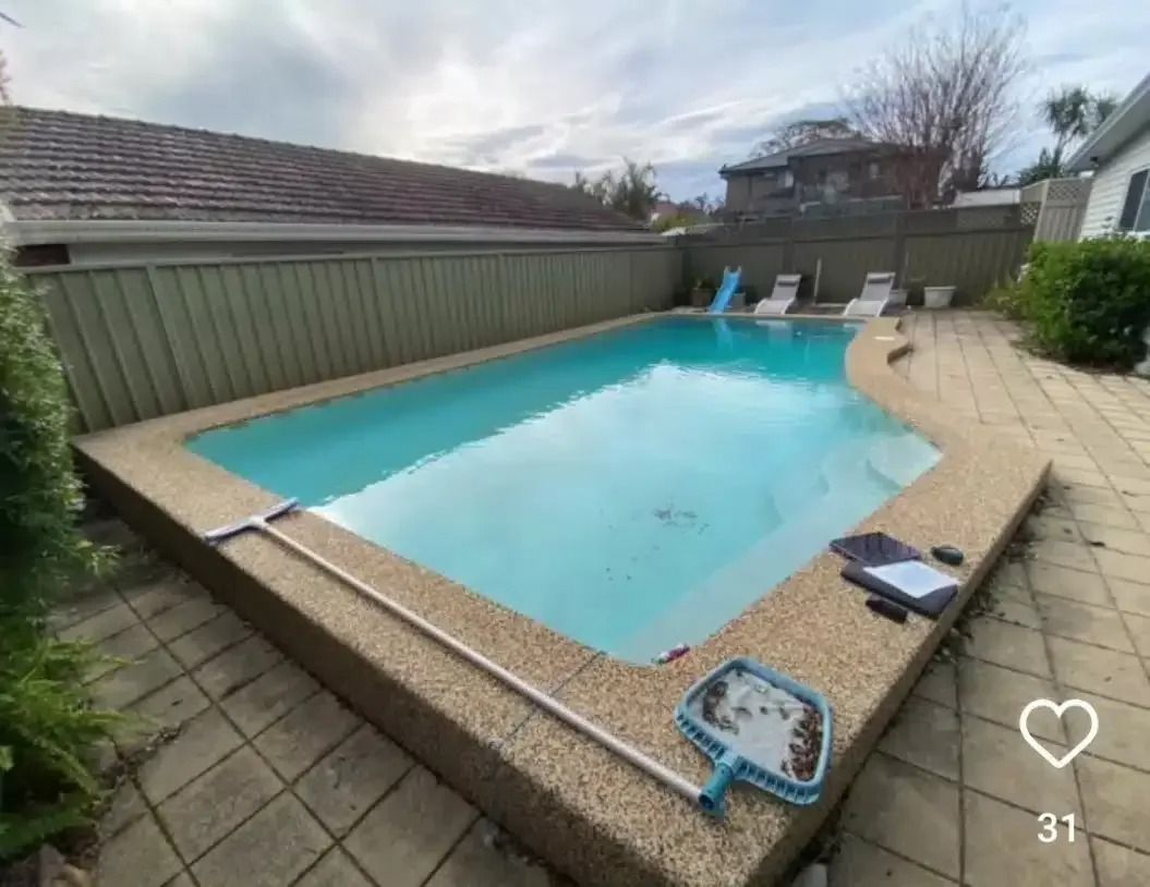 Swimming pool with beige concrete edging and a tan patio. A skimmer and other cleaning supplies are visible.