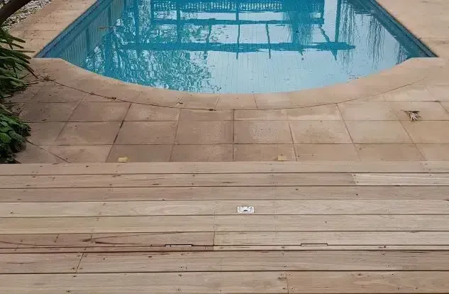 Wooden deck and stone patio leading to a rectangular pool with clear blue water.