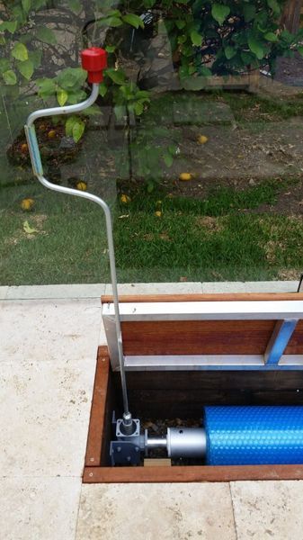 A hand crank mechanism in a box opens a blue pool cover.