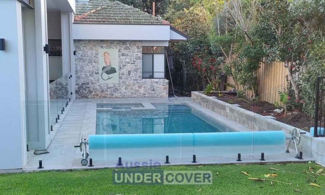 Swimming pool with blue cover, stone building, green grass, and trees.