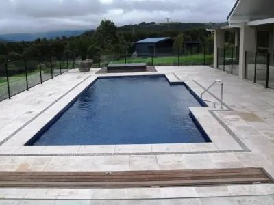 Rectangular blue swimming pool with stone surround, steps, and handrail. Includes a spa and fence.