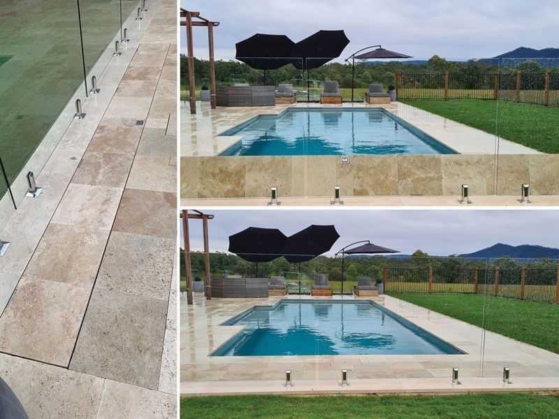 Poolside scene: glass fence, rectangular pool, stone tiles, black umbrella, and green lawn.