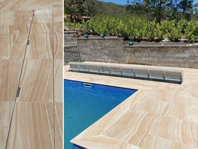 Pool deck with light brown stone tiles surrounding a blue swimming pool and a cover.