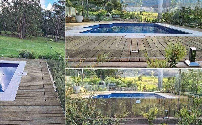 Swimming pool with wooden deck in a grassy outdoor setting, surrounded by greenery.