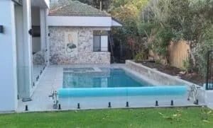 Swimming pool with blue cover, next to a stone building and lush greenery.