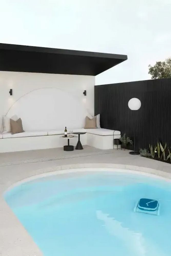 Poolside seating area with pool. White walls, black trim, neutral cushions, black table, and a pool cleaner.