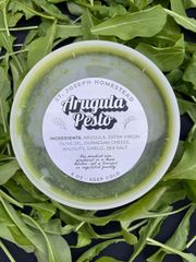 White-labeled green sauce container on a bed of leafy greens.