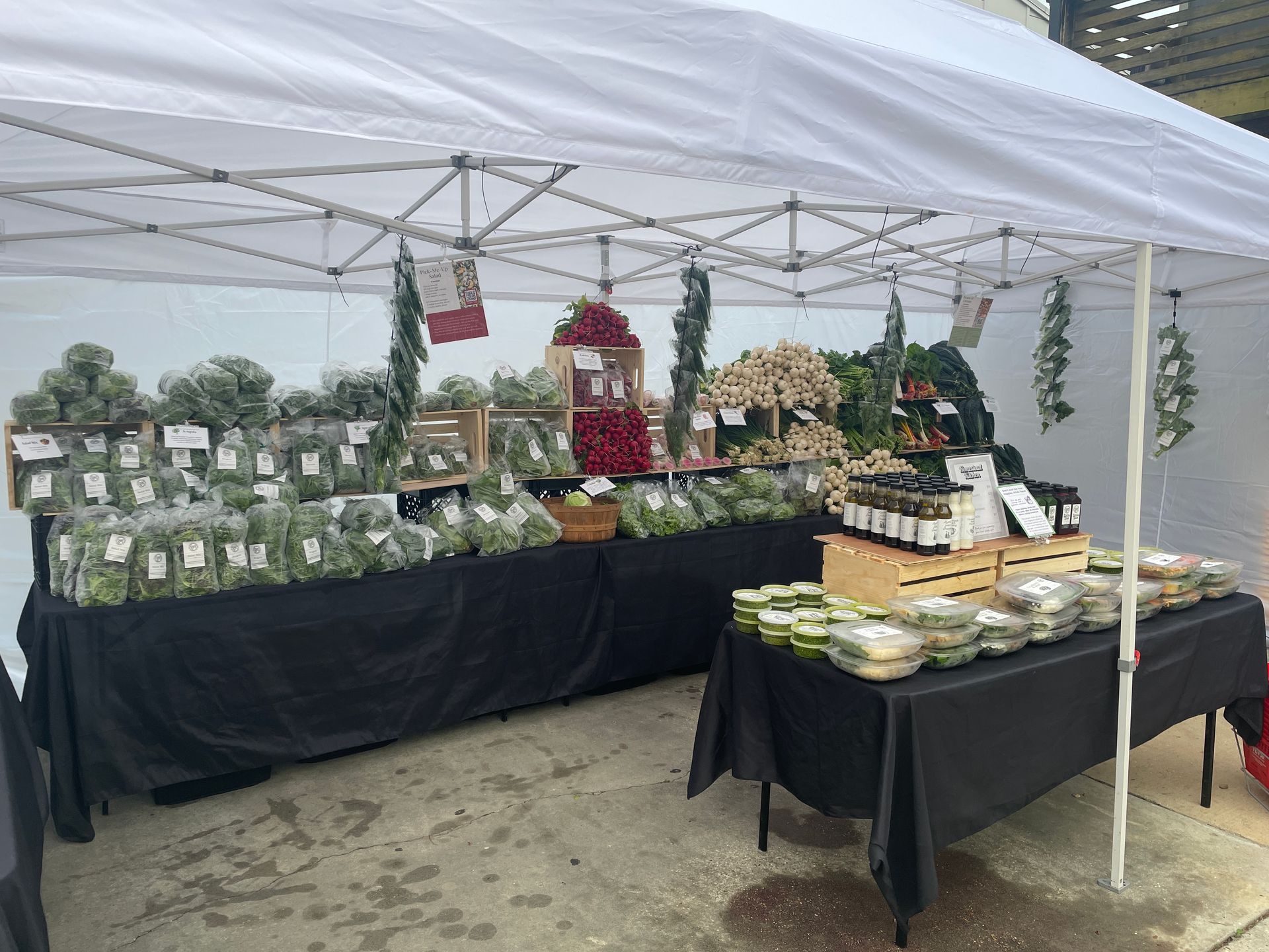 Outdoor market stall with black tablecloths displaying packaged goods and jars under a white canopy
