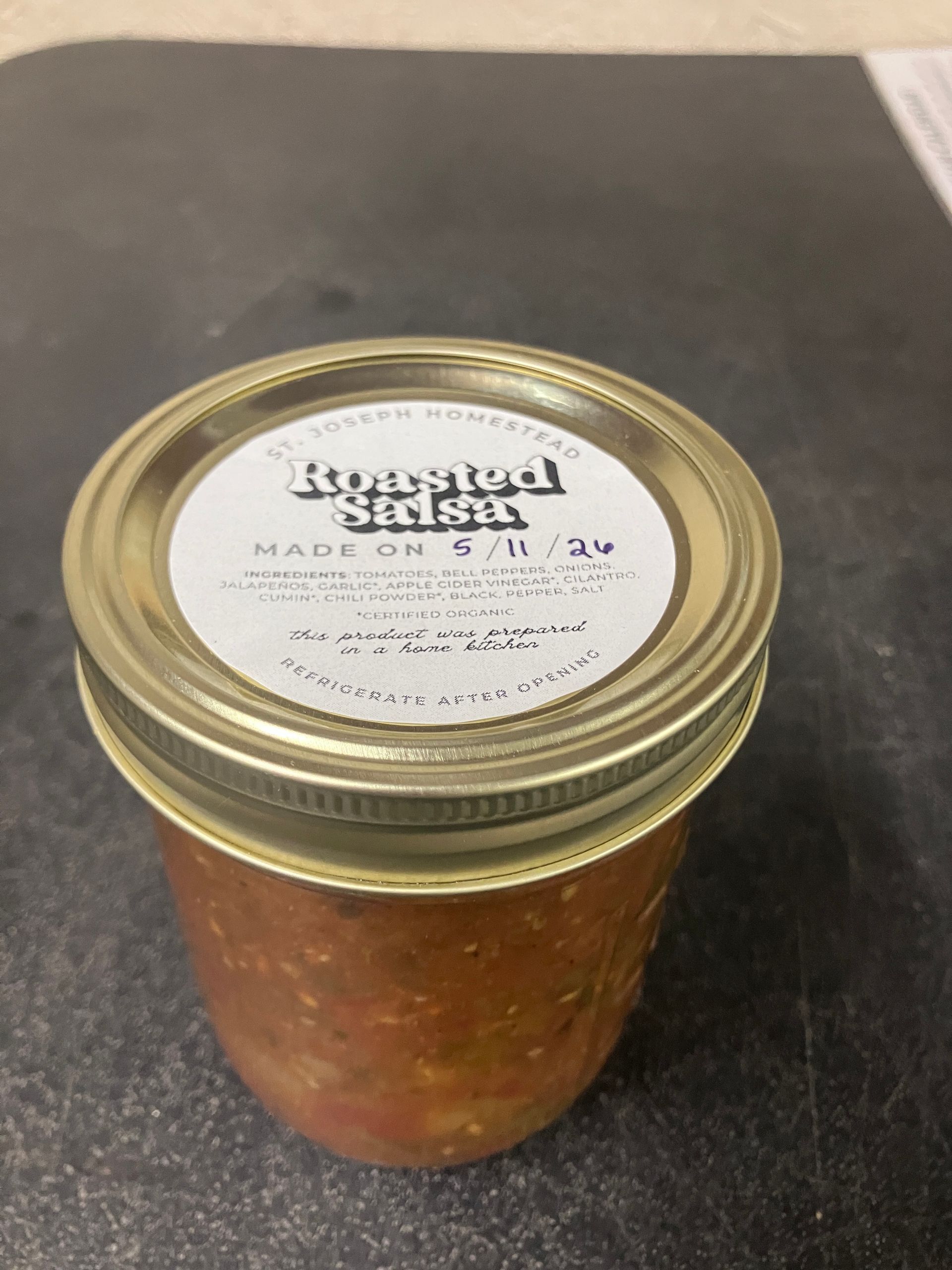 A jar of red salsa with a gold lid on a dark countertop.