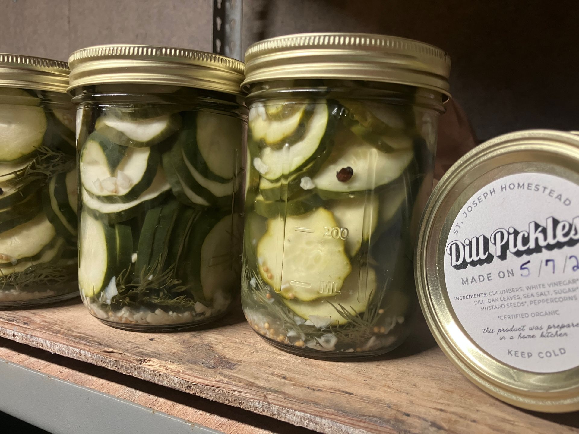 Three jars of pickles on a wooden shelf, one lid showing the label “Our Pickles.”