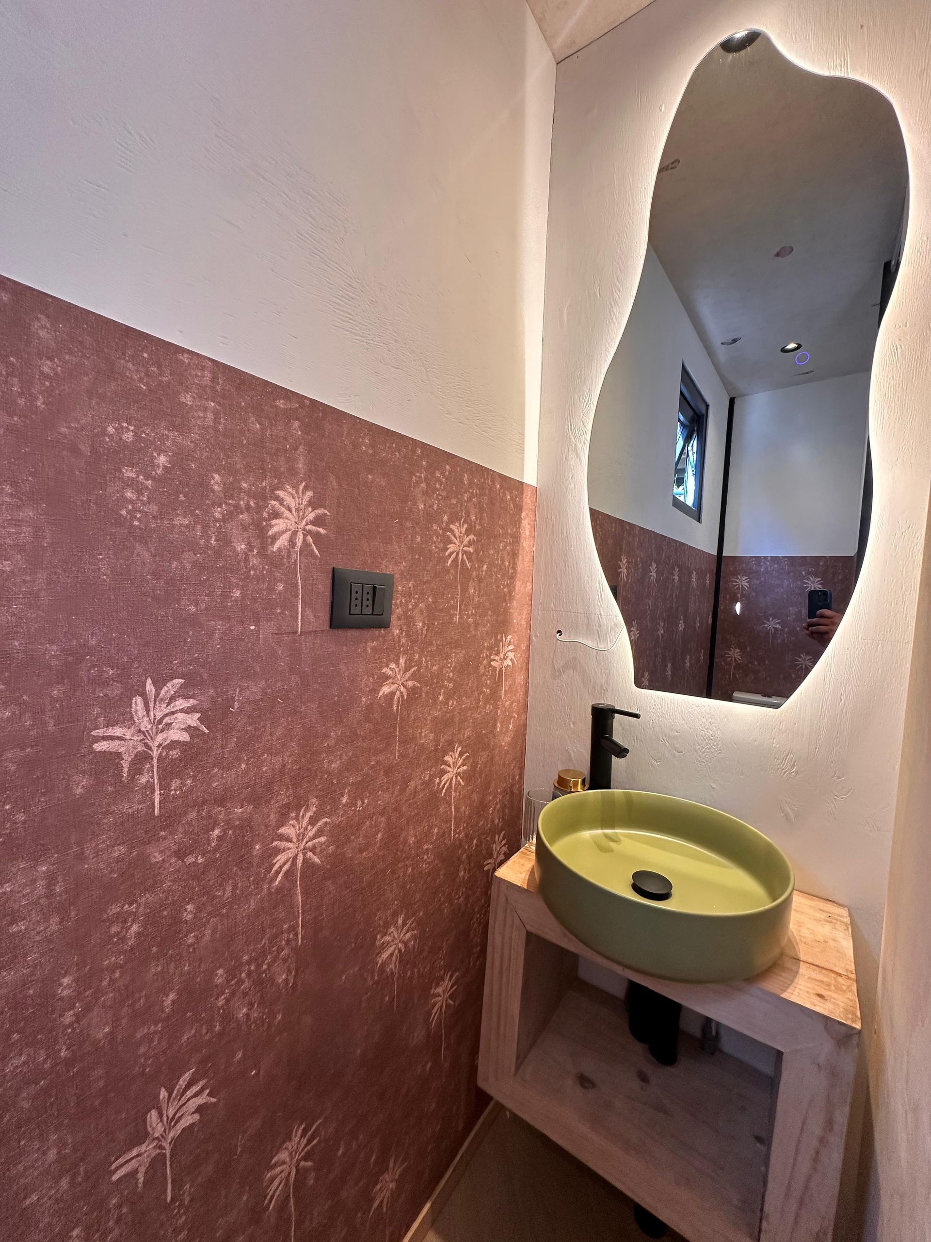 Small bathroom vanity with green sink, oval mirror, and pink textured walls with white floral patterns.