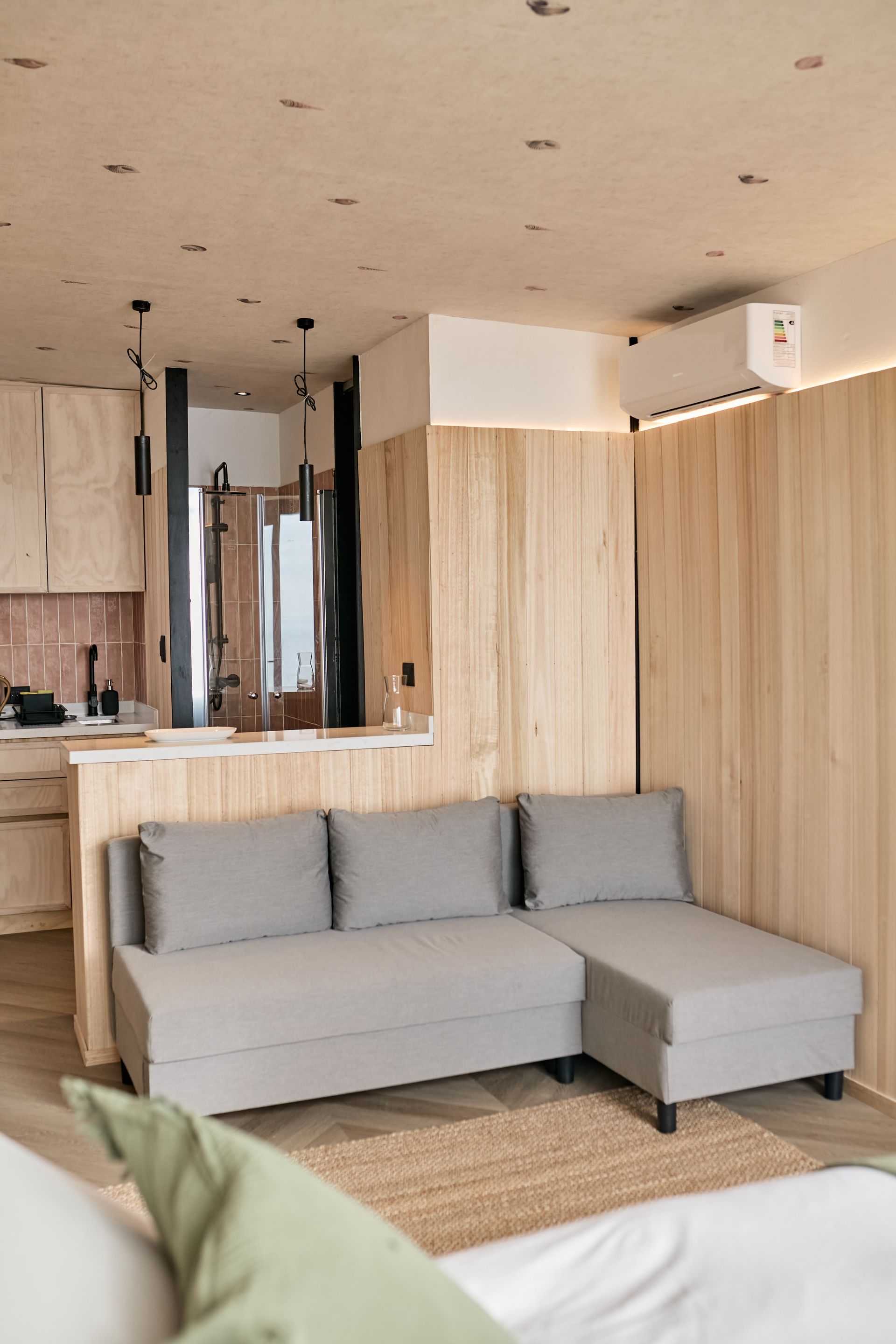 Modern living room with a light gray sectional, wood paneling, and open kitchen view