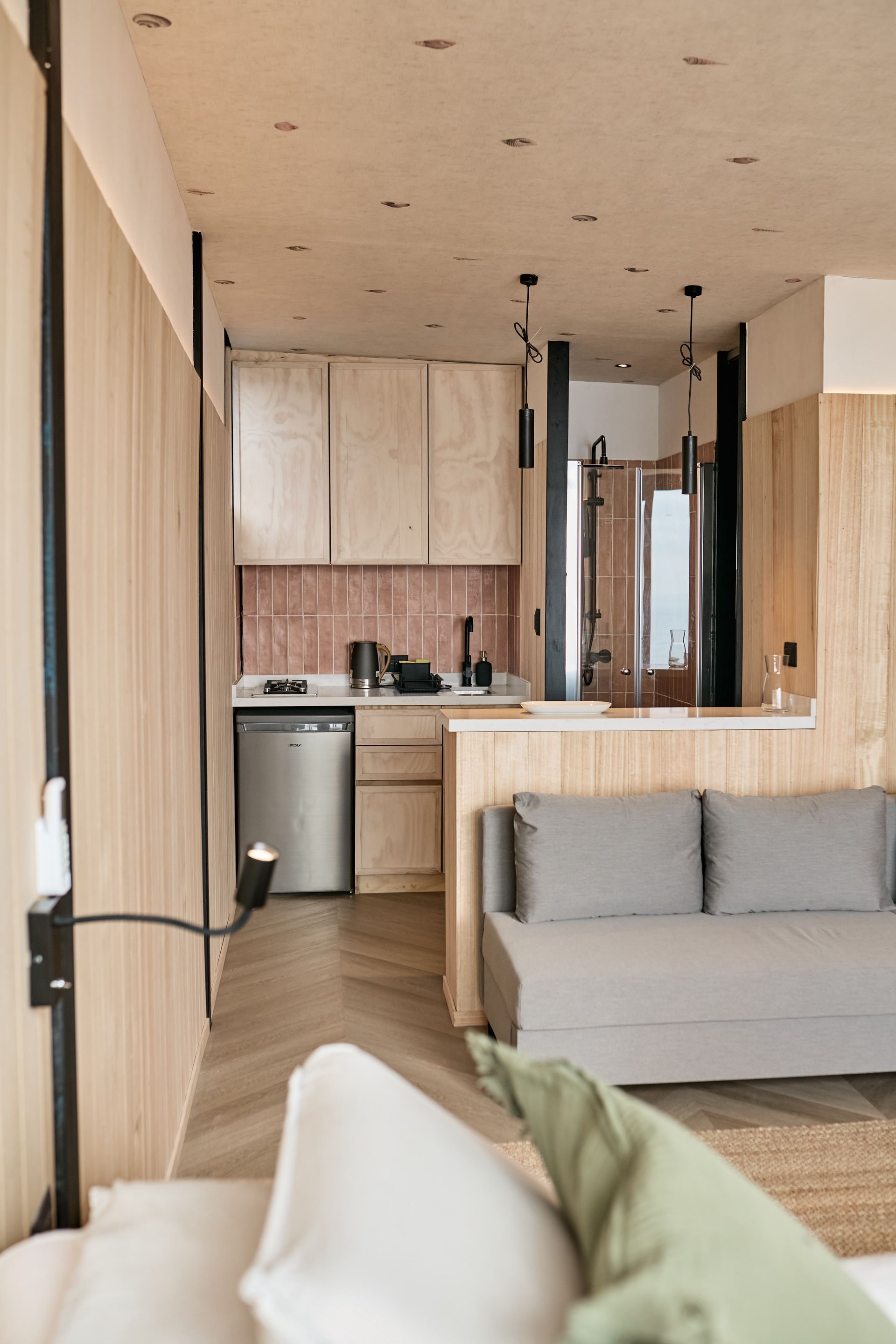 Modern apartment kitchen and living area with light wood finishes, gray sofa, and small dining nook