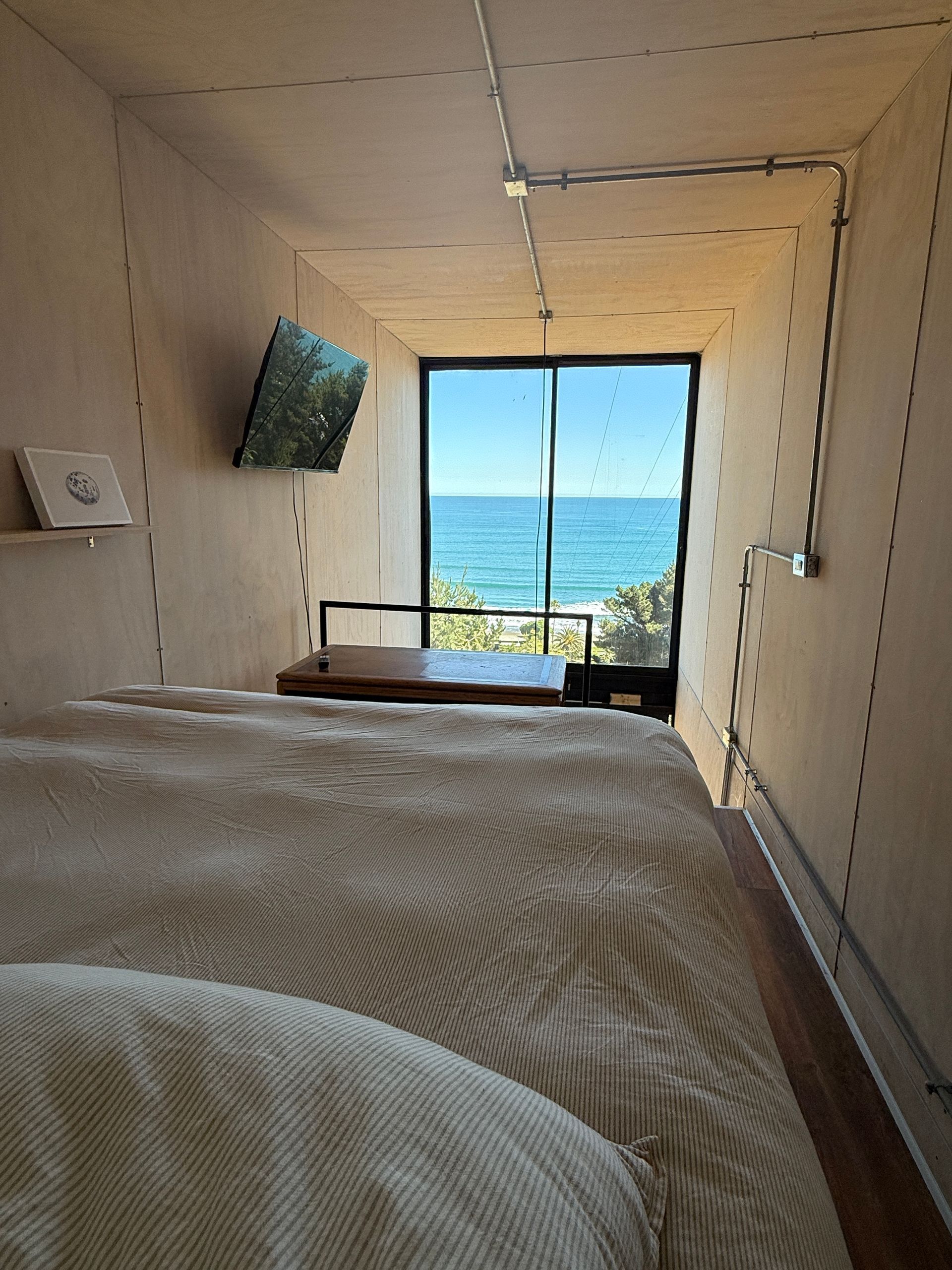 Cozy cabin bed facing a large window with ocean view and blue sky
