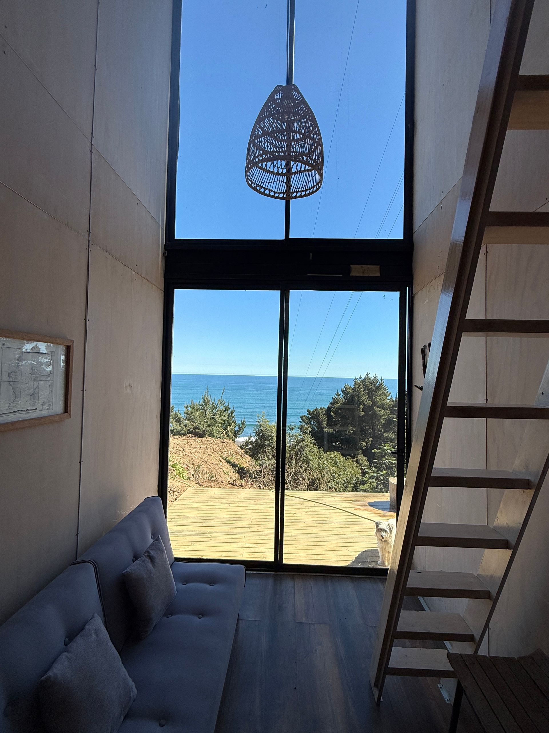 Modern loft interior with staircase, blue sofa, and large window overlooking ocean and lawn