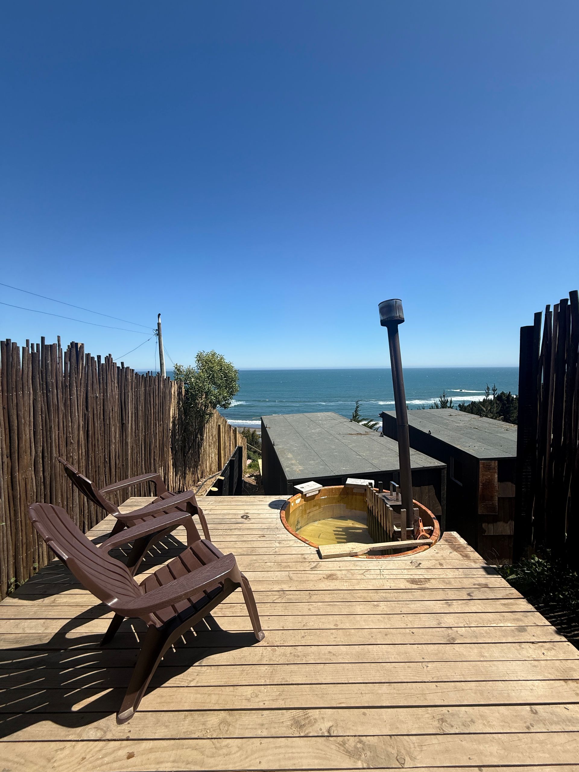 Wooden deck with lounge chairs overlooking the ocean under a clear blue sky