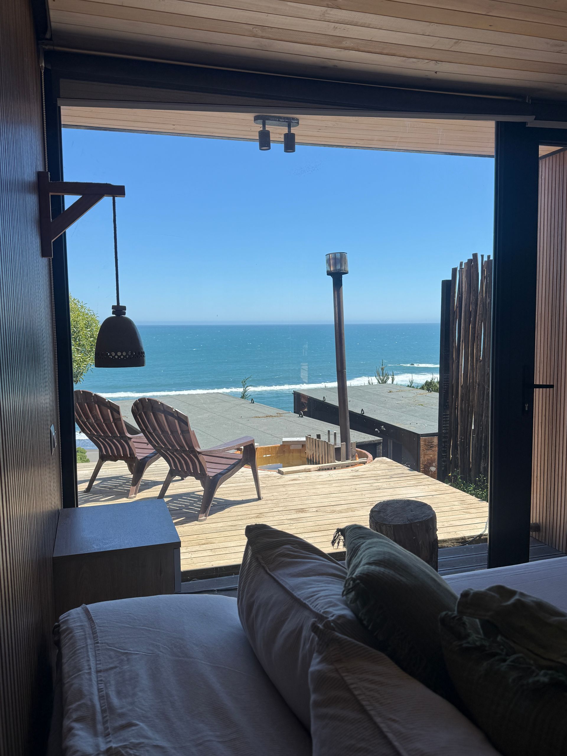 Seaside patio view through a doorway, with lounge chairs, ocean, and blue sky beyond.