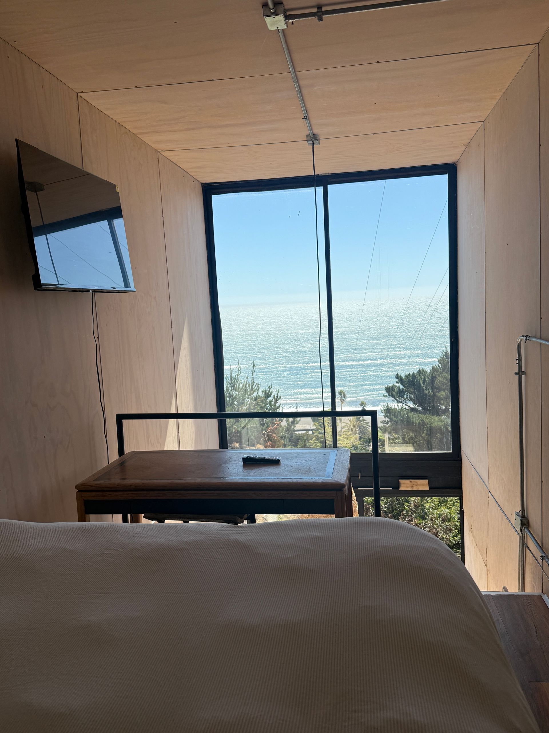 Modern room with bed, wall TV, desk, and large window overlooking the ocean