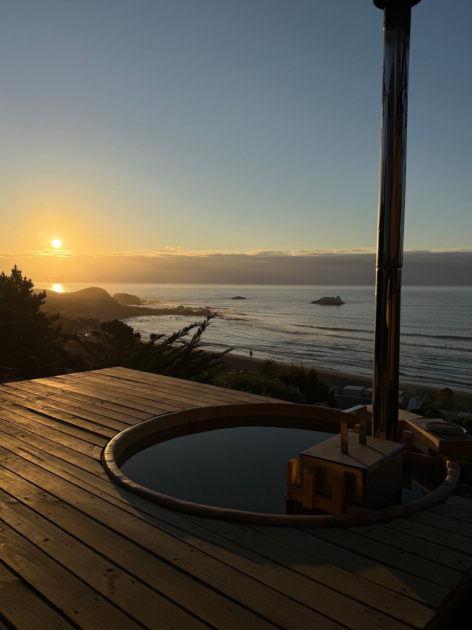 Sunrise over the ocean viewed from a wooden deck with a round hot tub in the foreground