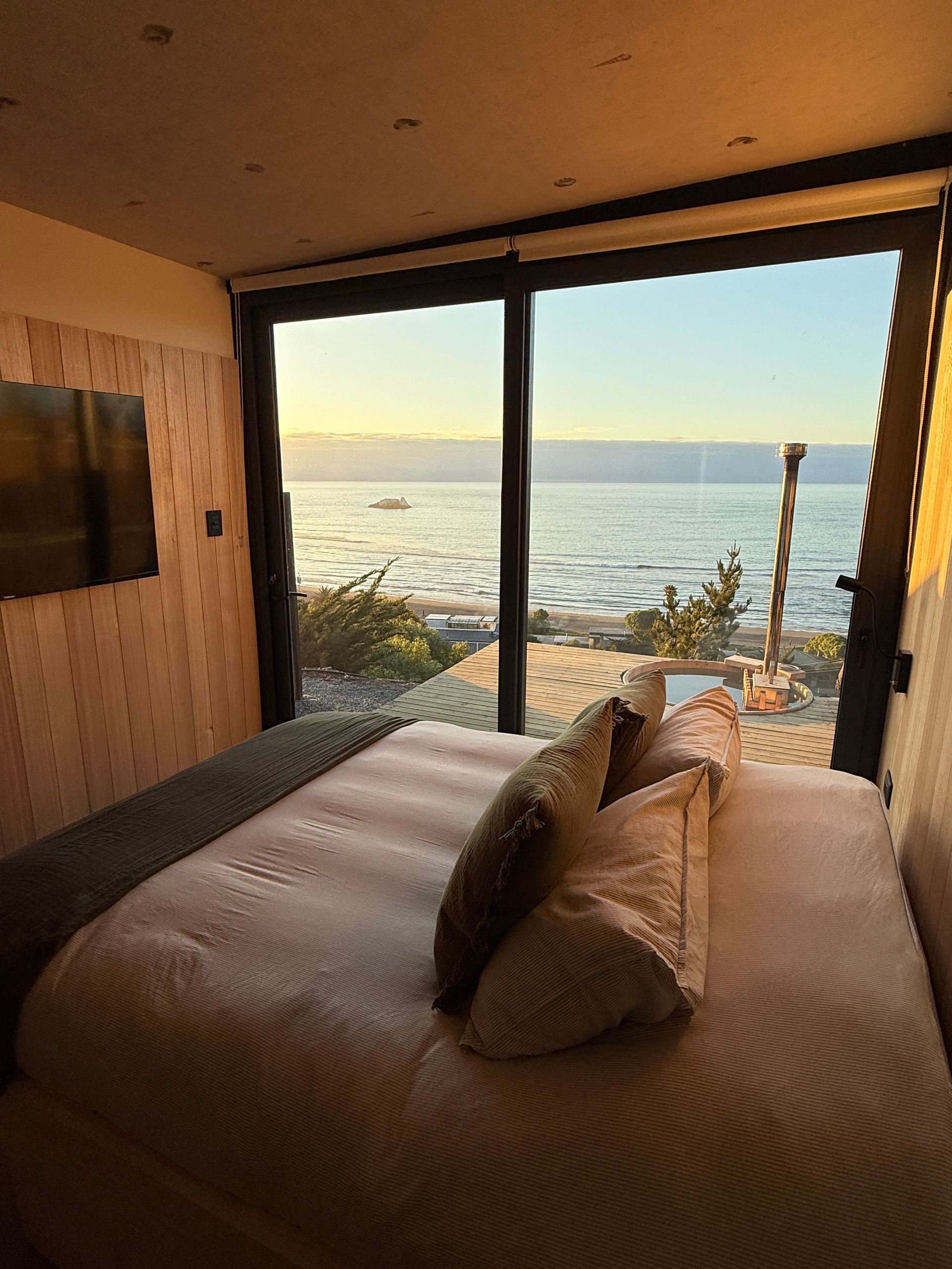 Modern bedroom with large windows overlooking a calm ocean at sunset