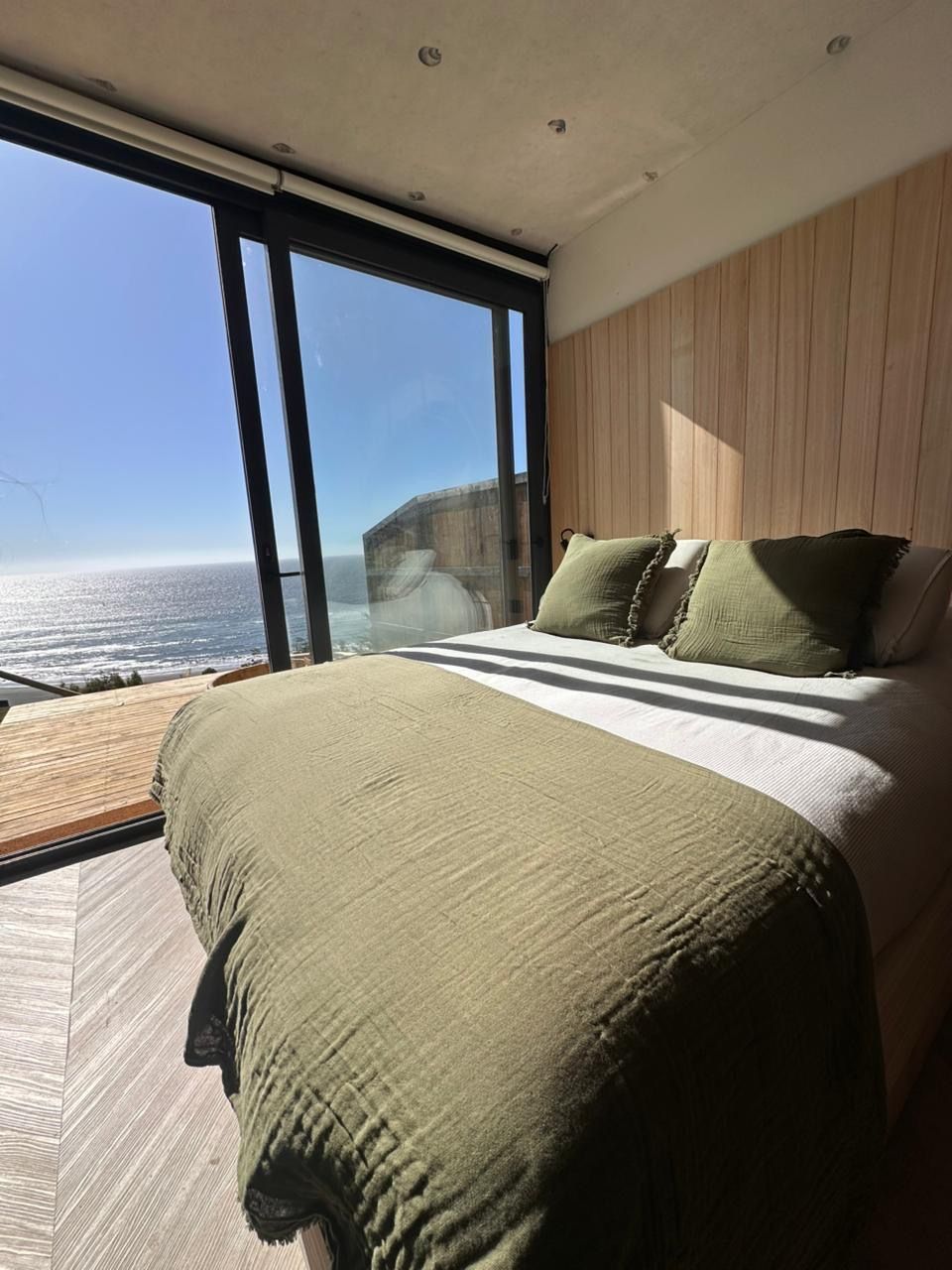 Sunlit bedroom with a bed by floor-to-ceiling windows overlooking the ocean and deck