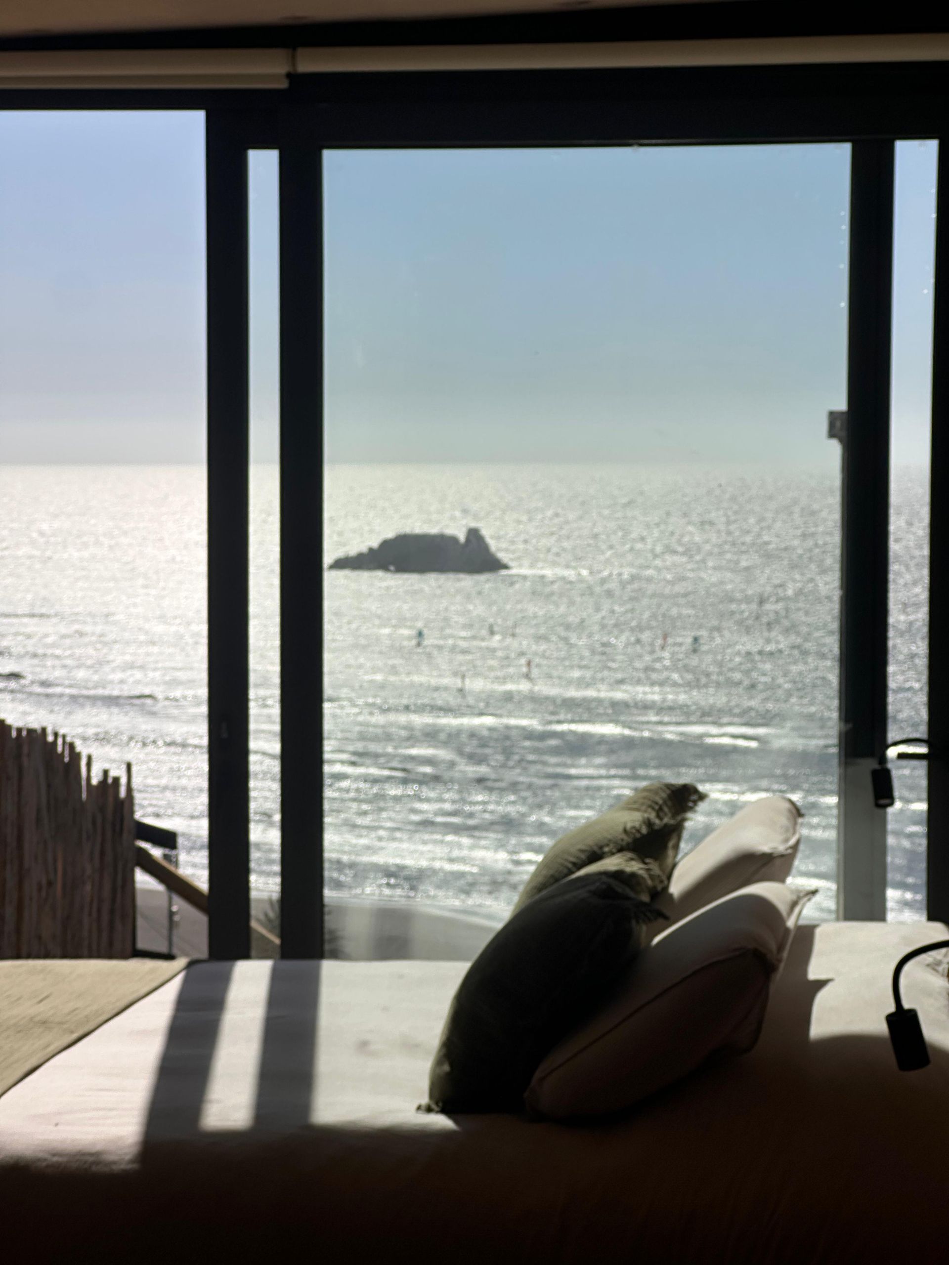 Beachfront room with bed and pillow facing a bright ocean view and small rocky island