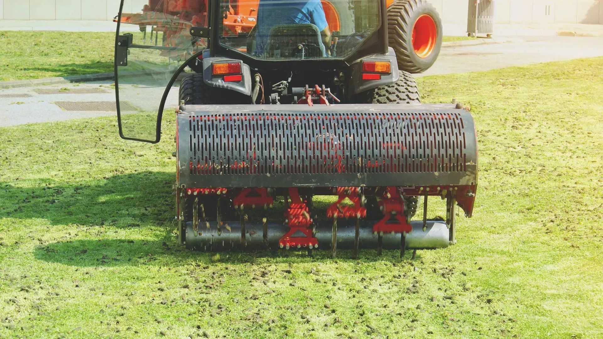 Tractor-mounted mower with a red roller cutting grass on a sunny green field