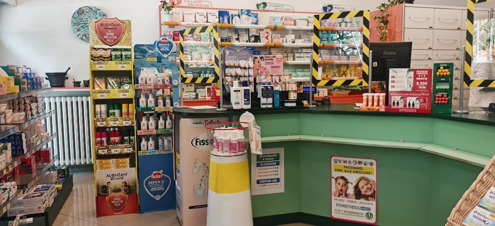 Bancone di un minimarket con caramelle, snack e bevande esposti su scaffali e un bancone cassa curvo di colore verde.