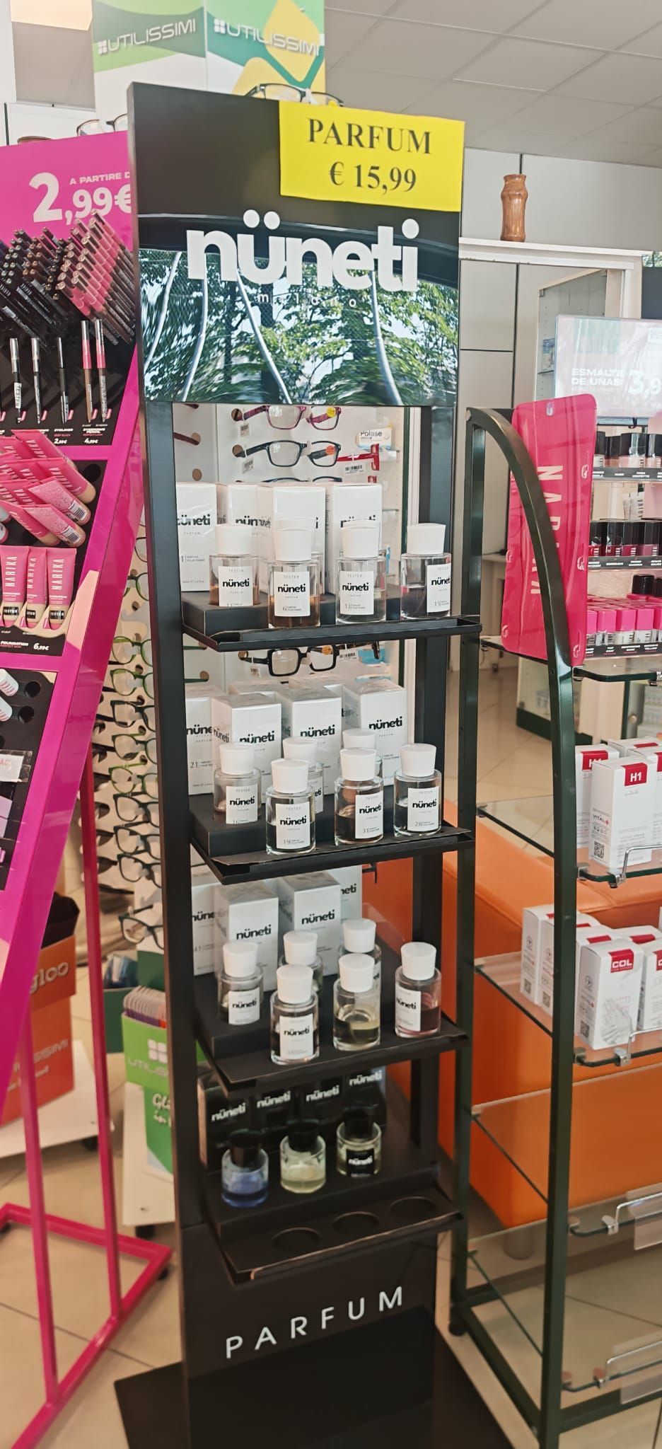 In un corridoio di un negozio, si trova uno scaffale nero per i prodotti per la cura della pelle NuNet, con flaconi di prodotti bianchi e rosa.
