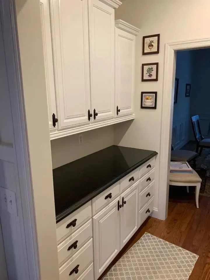 A kitchen with white cabinets and black counter tops.
