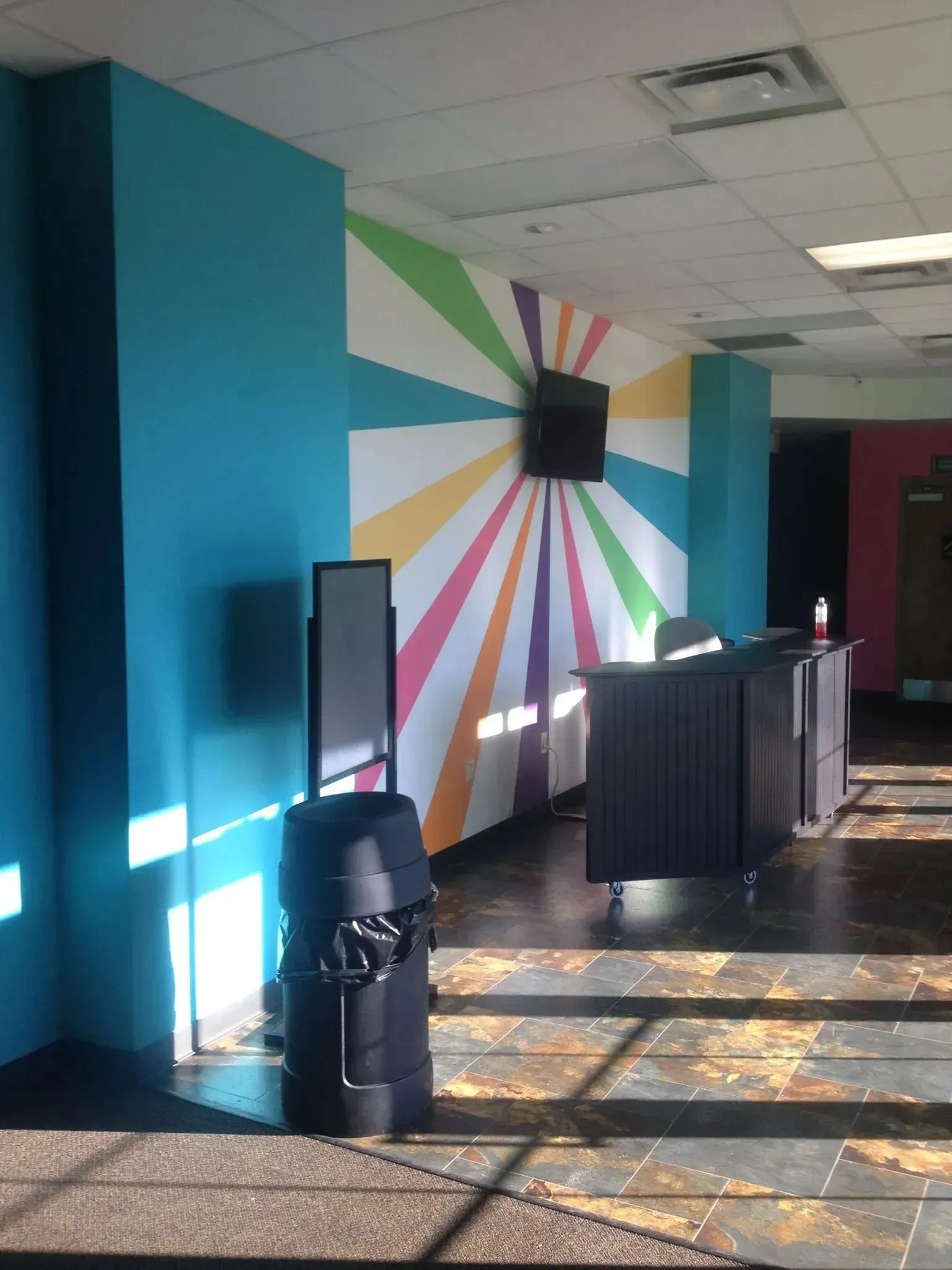A room with a rainbow painted wall and a black trash can