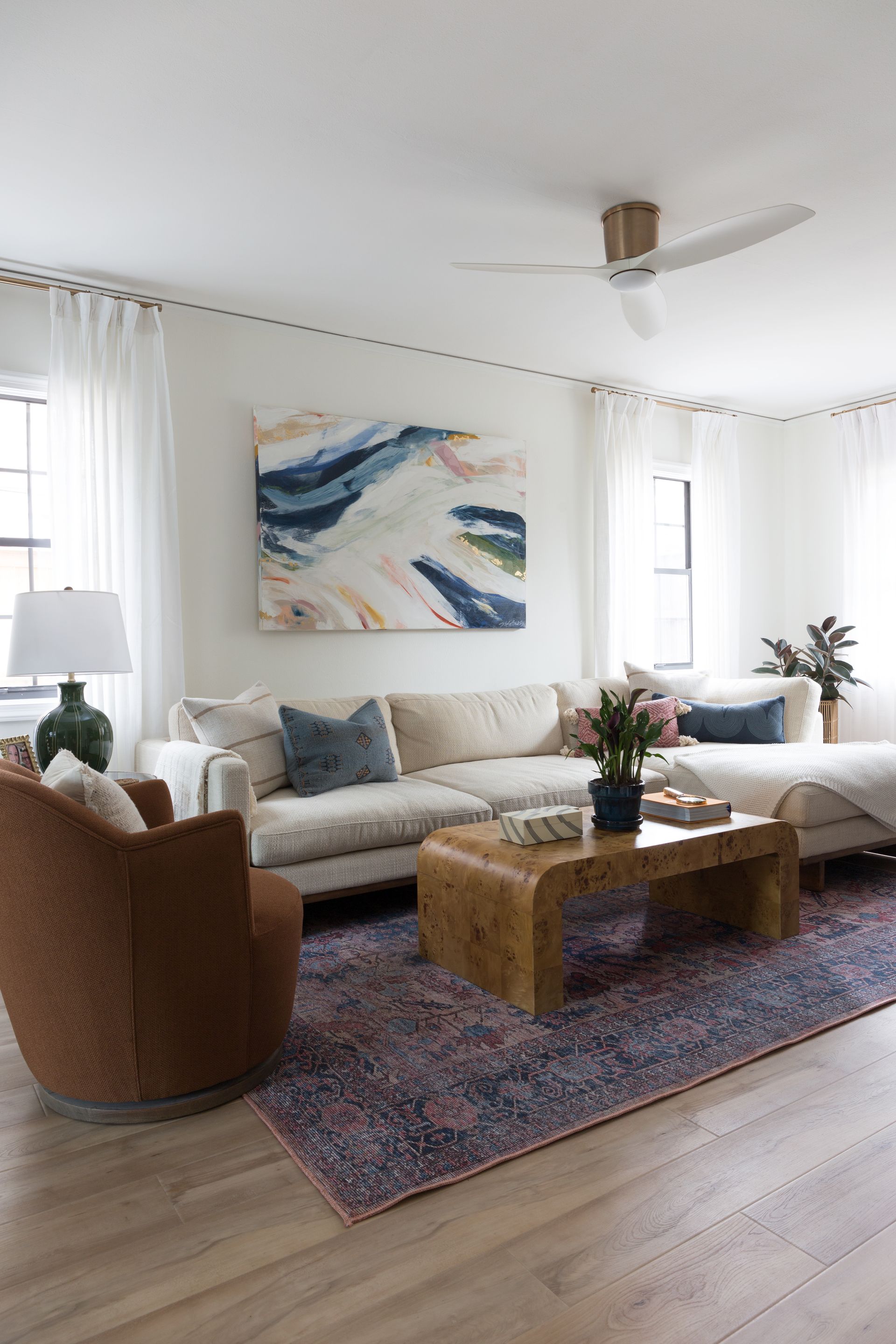 Two light-colored armchairs with decorative pillows, a dark ottoman, and two lamps against a teal wall.