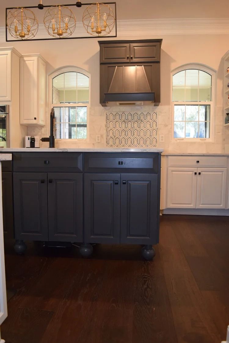 Kitchen with dark gray island, white cabinets, and wood flooring.