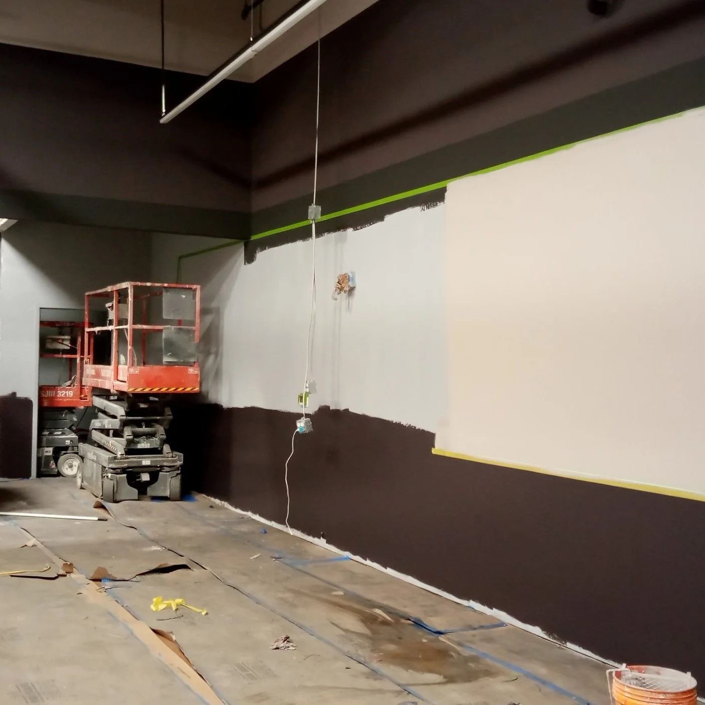 Interior under renovation, partially painted dark brown and gray walls. A lift is present.