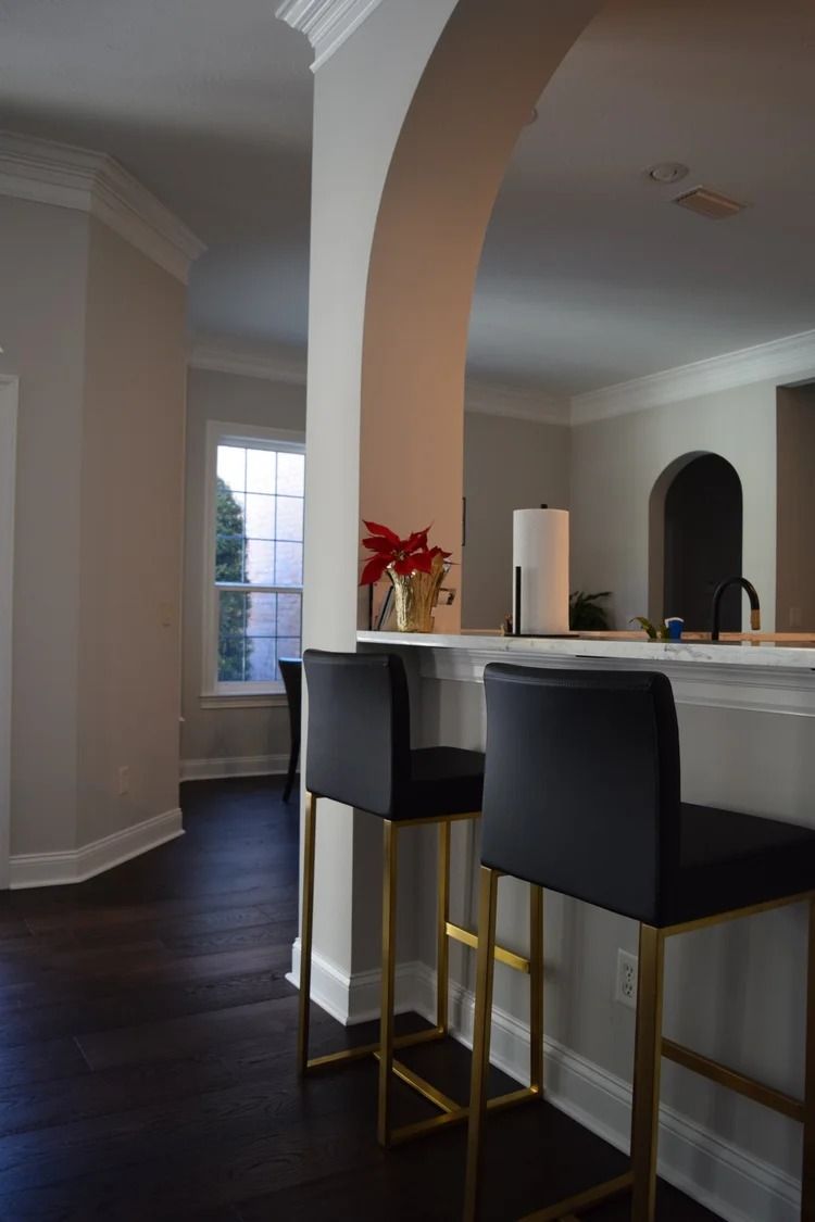 Interior with bar stools at a counter, archway, dark wood floor.