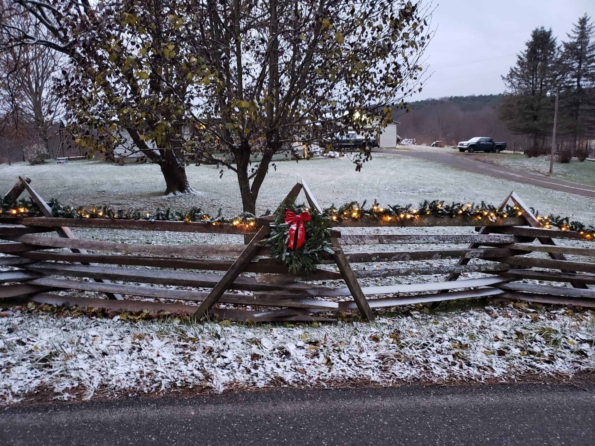 Snow-dusted wooden fence with holiday wreaths beside a frozen pond and trees in a winter landscape